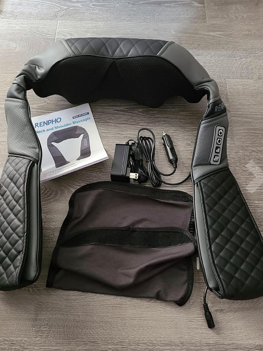 A RENPHO neck and shoulder massager is displayed with a manual, power adapter, car charger, and carrying case on a wooden floor. This versatile set complements your collection of massage guns perfectly.