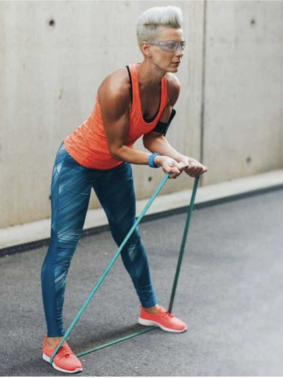 A person wearing athletic gear performs a resistance band exercise, standing on the band with knees slightly bent and pulling the band upwards. After their workout, they use massage guns to soothe sore muscles and enhance recovery.