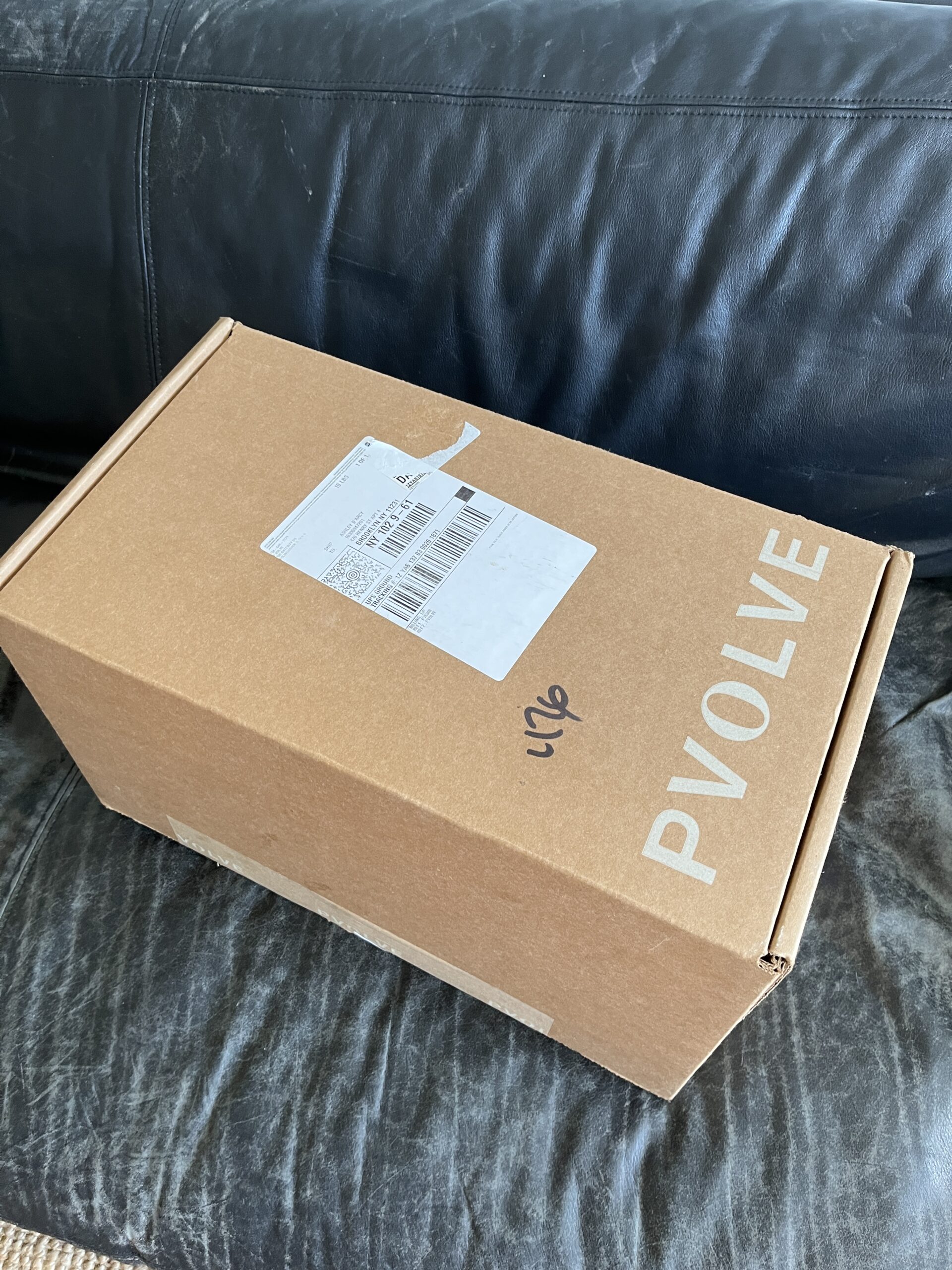 A sealed Pvolve cardboard box with a shipping label sits on a black leather surface.