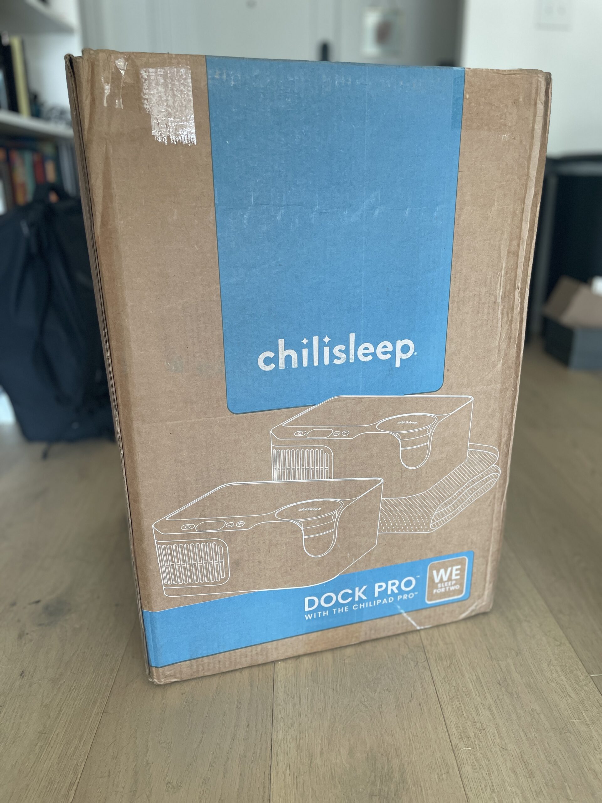 A cardboard box labeled "chilisleep Dock Pro" is placed on a wooden floor. The box features an illustration of two devices and a blue section with branding.