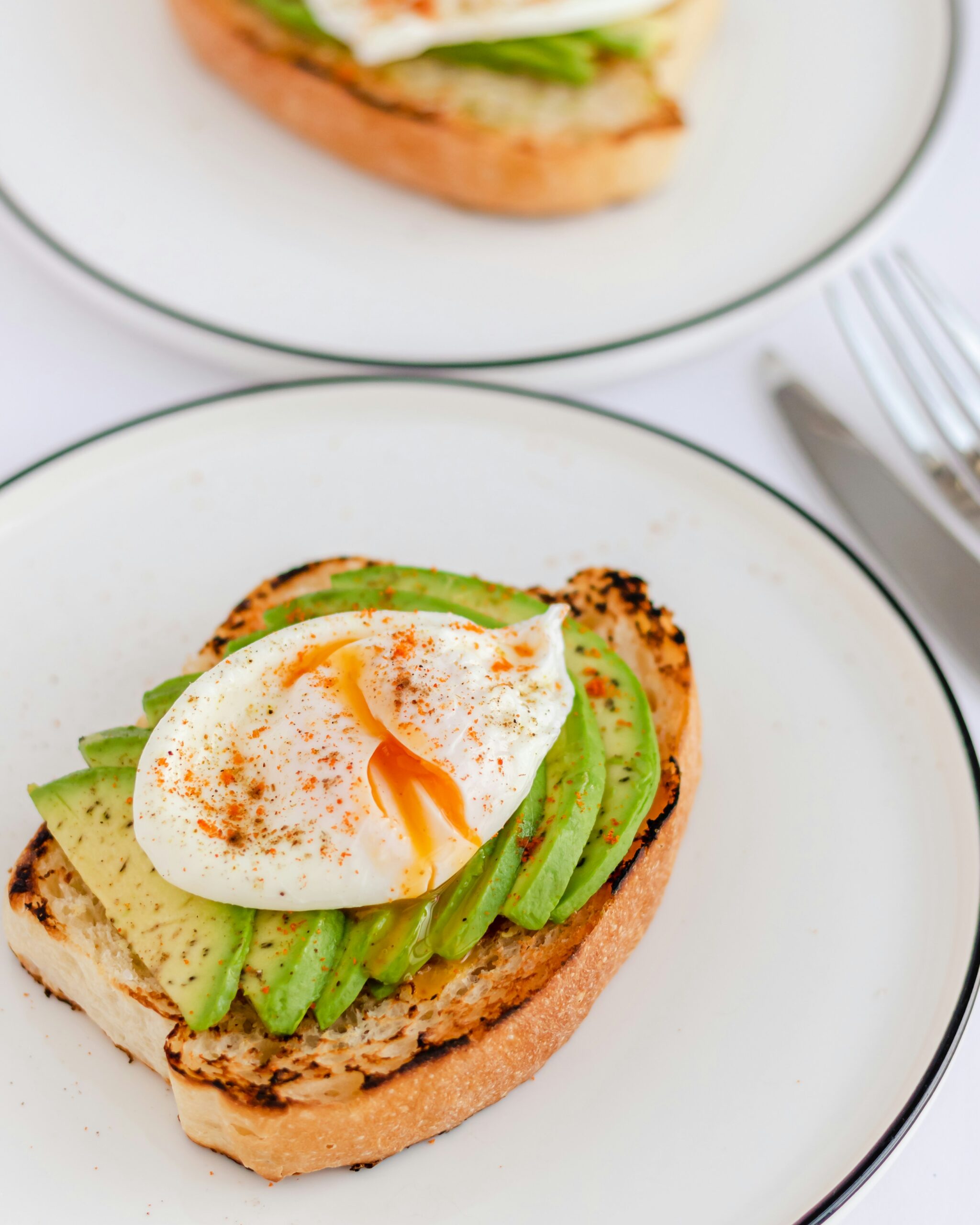 A plate with a slice of toast topped with avocado slices and a poached egg, seasoned with paprika.