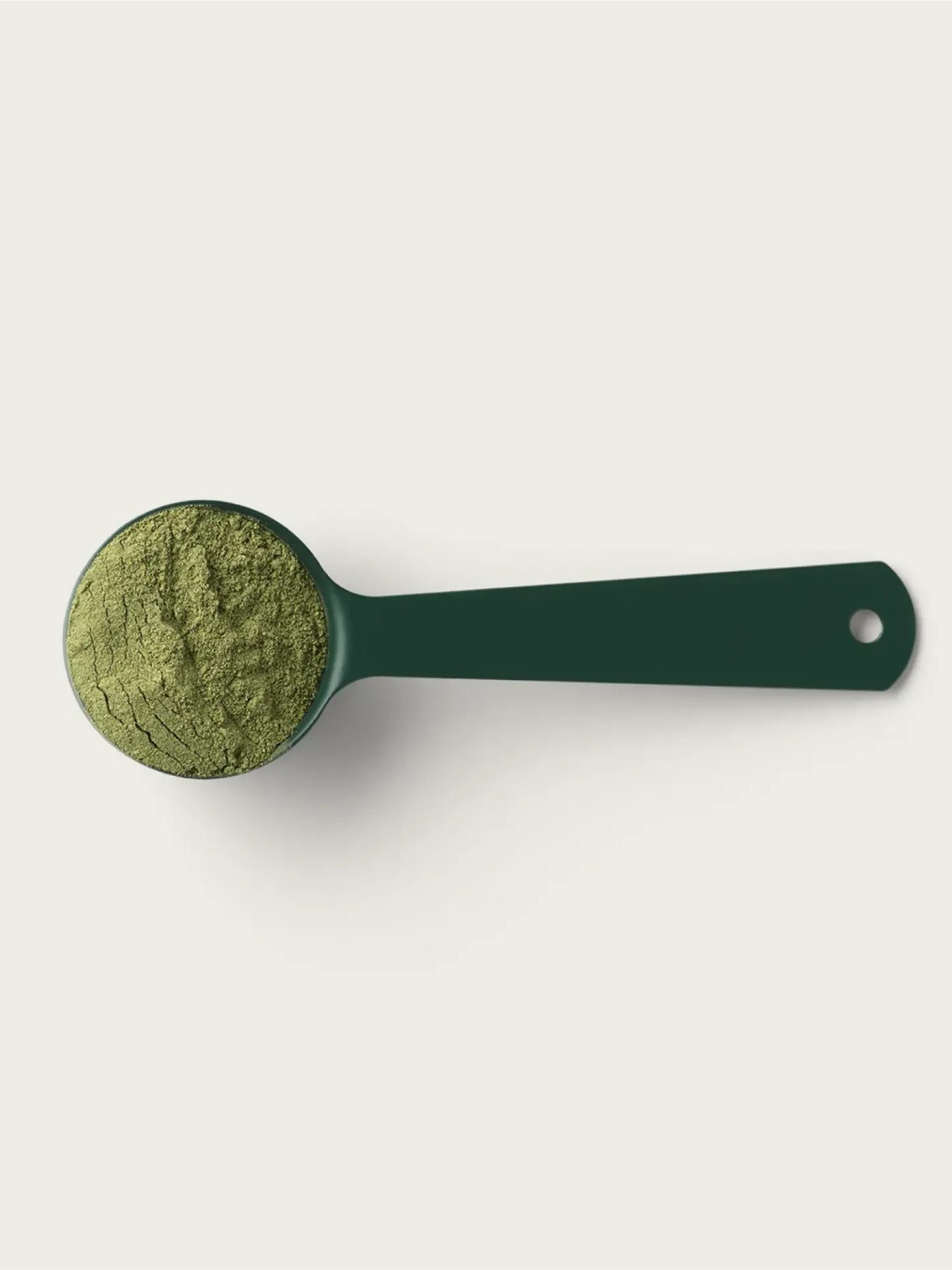 A green measuring scoop filled with green powder rests on a pale background.