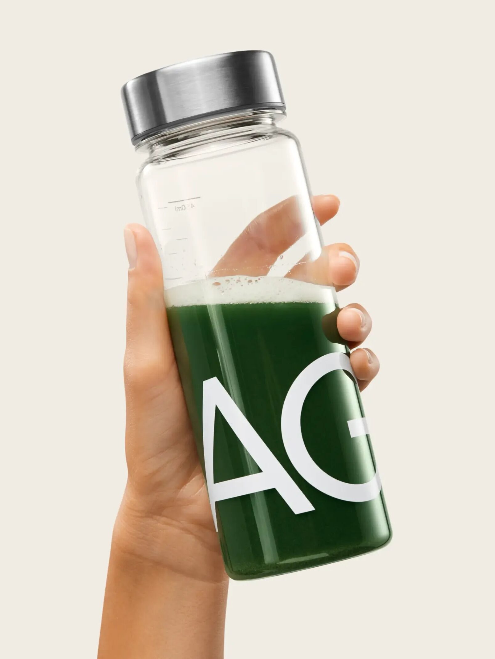 A hand holds a clear bottle with a silver lid, containing vibrant green liquid. 