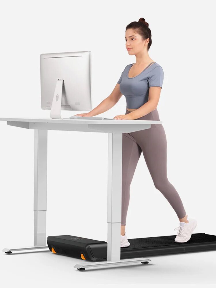 A woman walks on a treadmill while working at a standing desk with a computer.