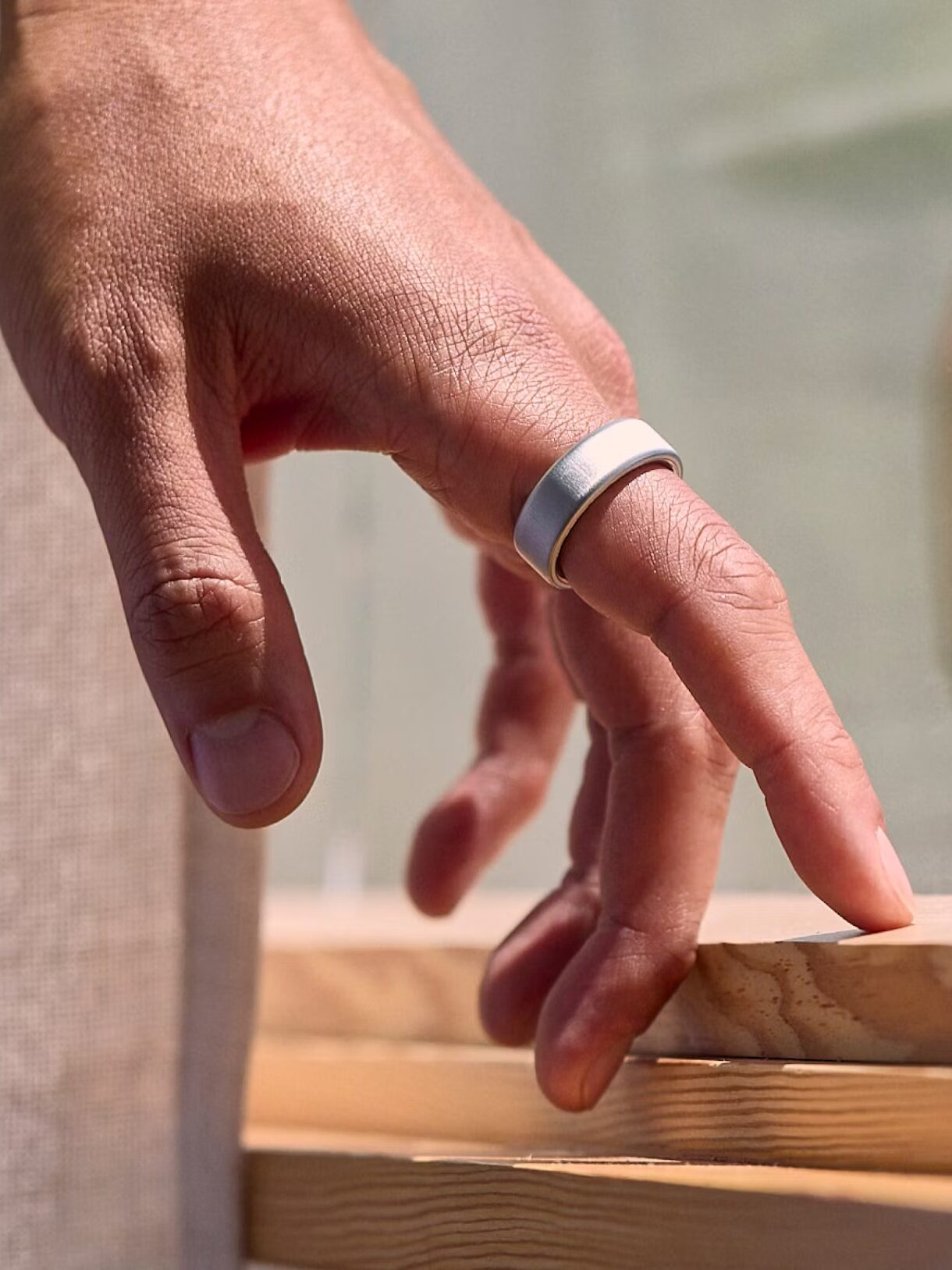 A hand adorned with a silver ring lightly touches a wooden window frame.