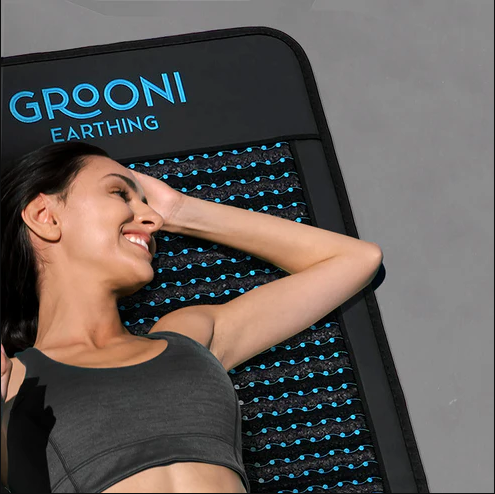 A person smiles contentedly while lying on a Grooni earthing mat, as soothing as a session with massage guns.