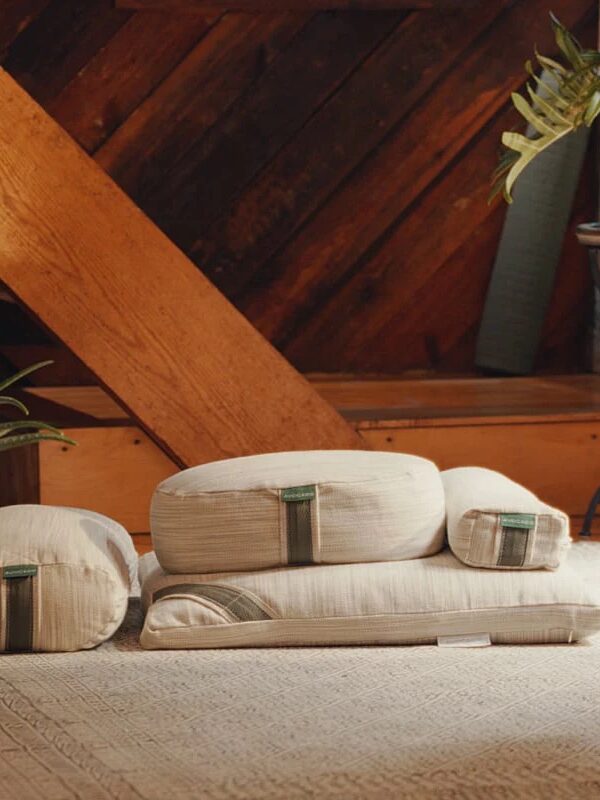 A set of beige yoga cushions and a folded mat are arranged on a wooden floor.