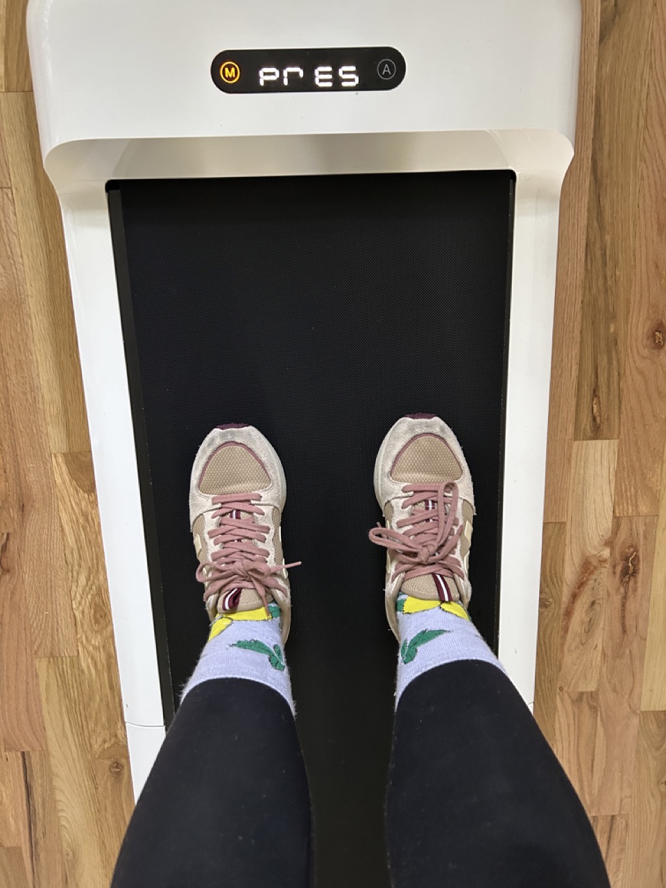 Person stands on a treadmill, wearing pink sneakers and socks with lemon patterns.