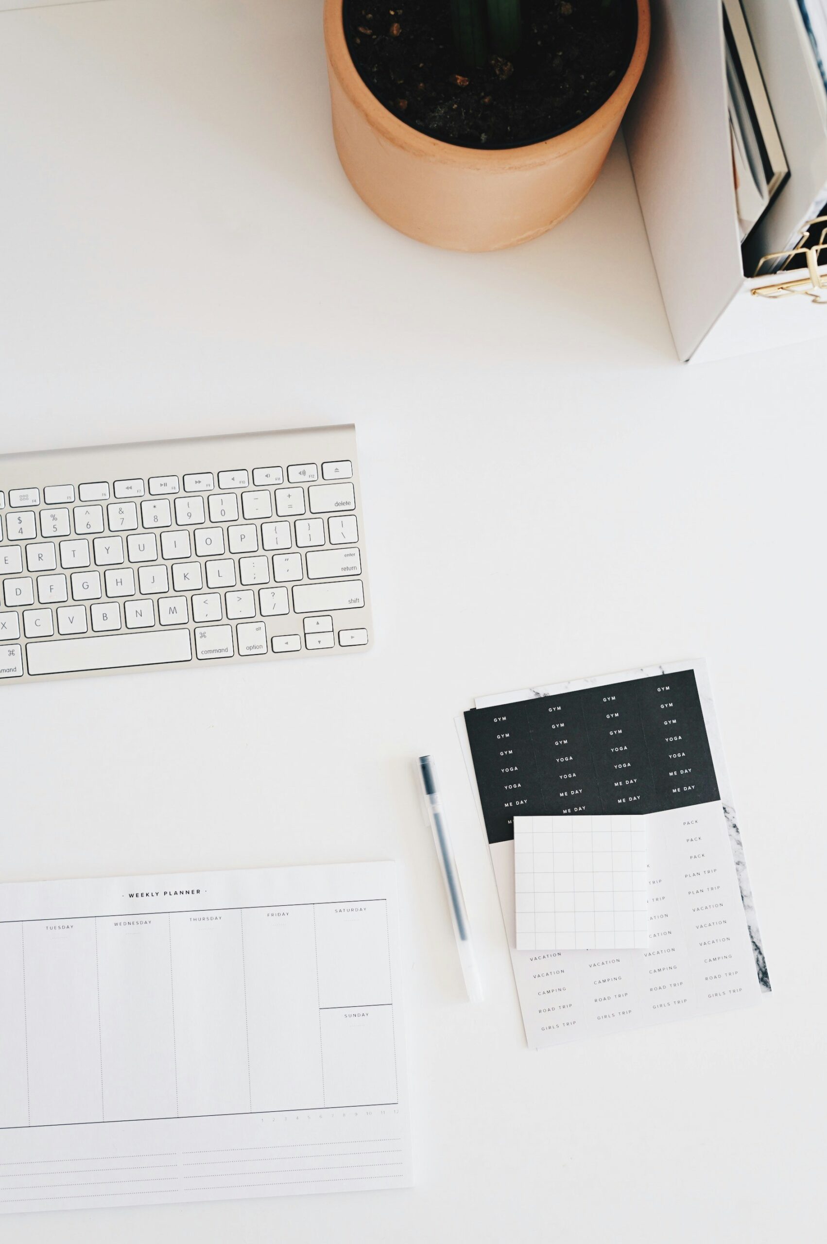 A white desk with a computer keyboard, a pen, a potted plant, a planner, and a calendar.