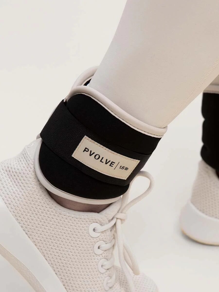 A person sporting ankle weights labeled "Pvolve" with white leggings and sneakers, perfectly prepared for a workout enhanced by massage guns.