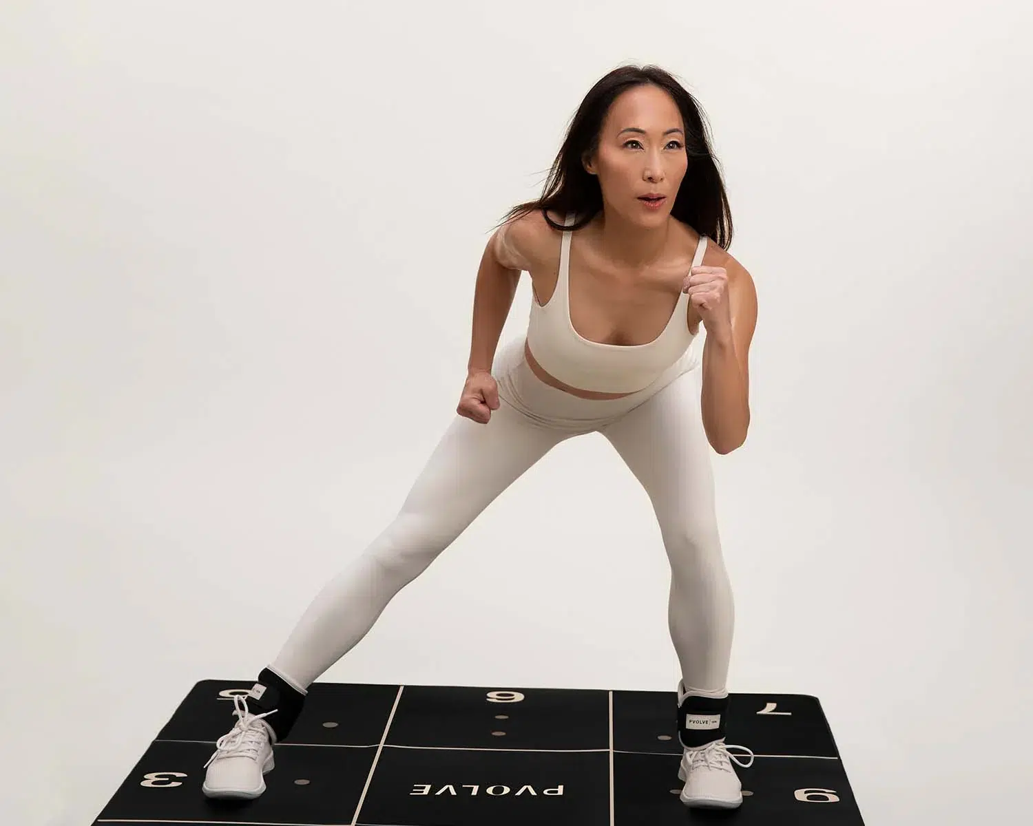 A person in athletic wear performs a dynamic exercise on a numbered workout mat, wearing ankle weights.