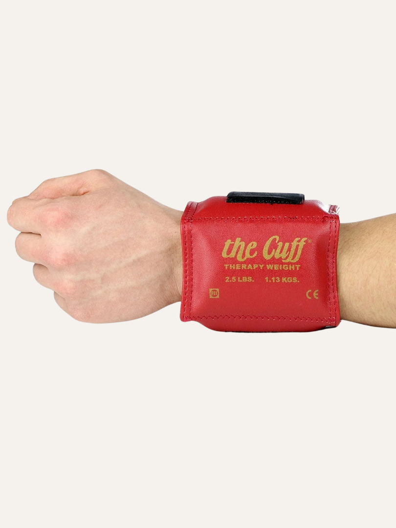 A wrist adorned with "the Cuff," a red therapy weight of 2.5 lbs (1.13 kgs), complements the relief provided by versatile massage guns, enhancing recovery and strength.