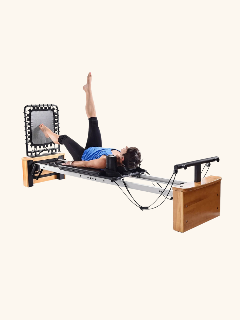 A person is exercising on a Pilates reformer machine, performing a leg raise with one leg extended upward. Nearby, massage guns offer soothing relief for muscles post-workout.