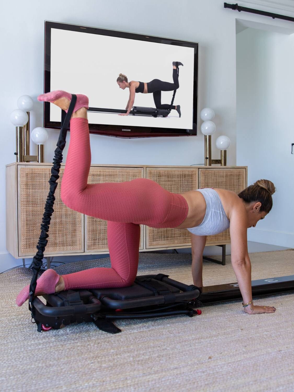 A person is exercising with resistance equipment in a room, seamlessly following a workout video displayed on a wall-mounted TV. Nearby, massage guns await their post-workout role to soothe and relax tired muscles.