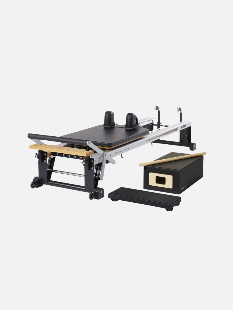 A Pilates reformer machine featuring an attached box, jump board, and platform extension sits on a white background, ready to complement your workout with massage guns for ultimate relaxation.