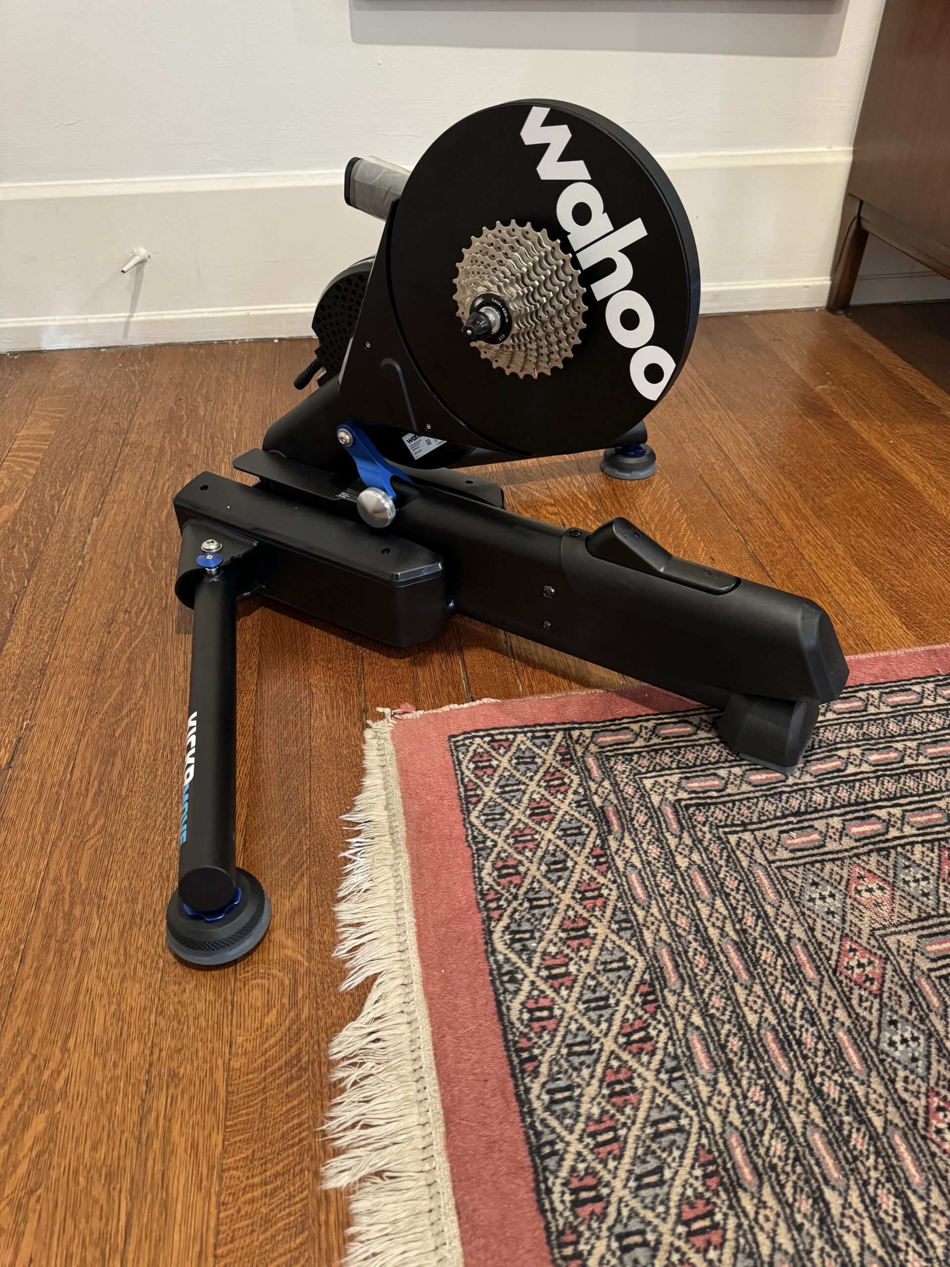 A Wahoo indoor bike trainer is set up on a wooden floor next to a rug.