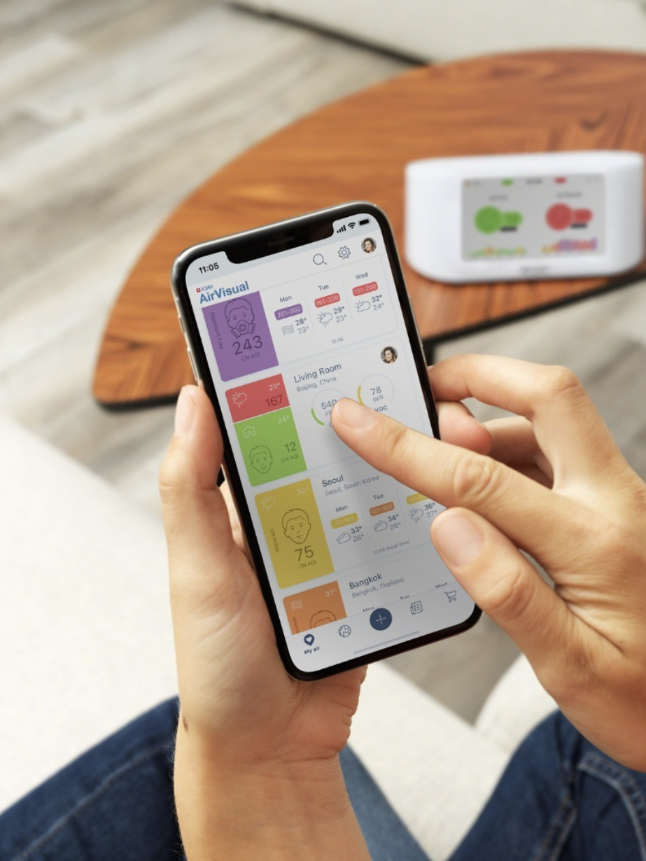 A person is seated on a couch, holding a smartphone that displays air quality information.