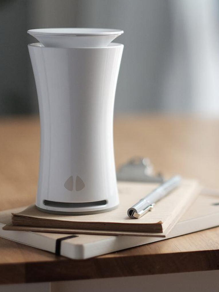 A white air quality monitor sits on a wooden table next to a notepad.