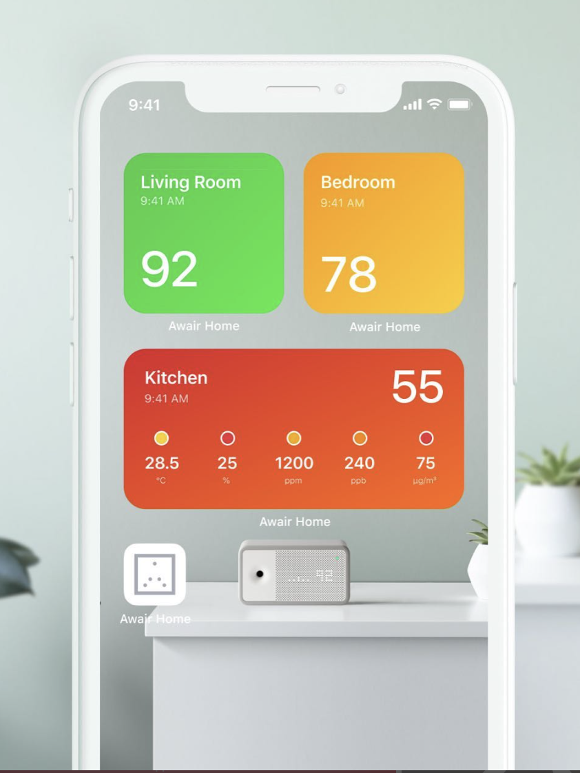 A smartphone displaying a home air quality app, with ratings for Living Room 92, Bedroom 78, and Kitchen 55, rests on a table adorned with decor items.