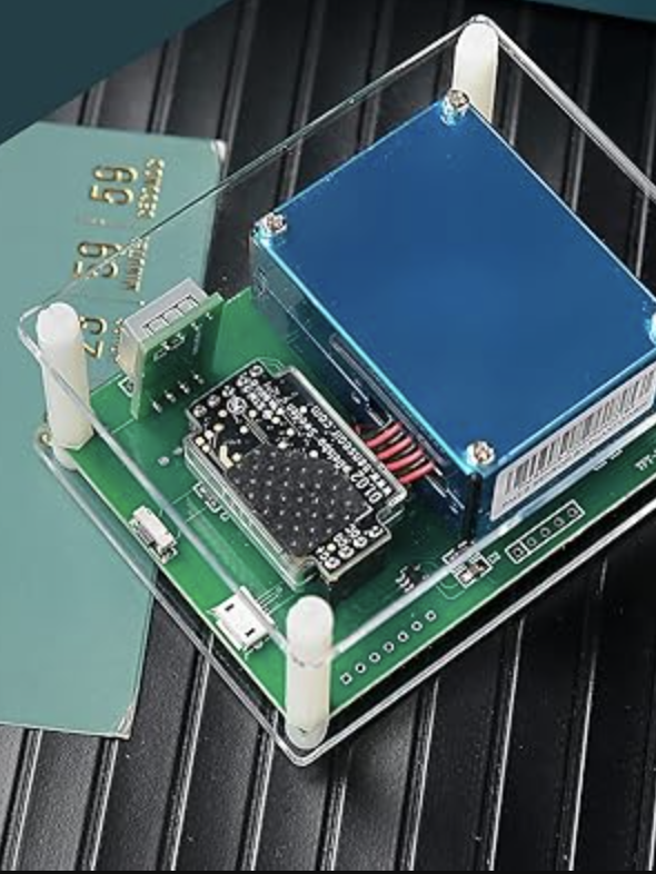 A small electronic device, features a blue component on a green circuit board. It's enclosed in a transparent casing and rests on a dark ribbed surface.