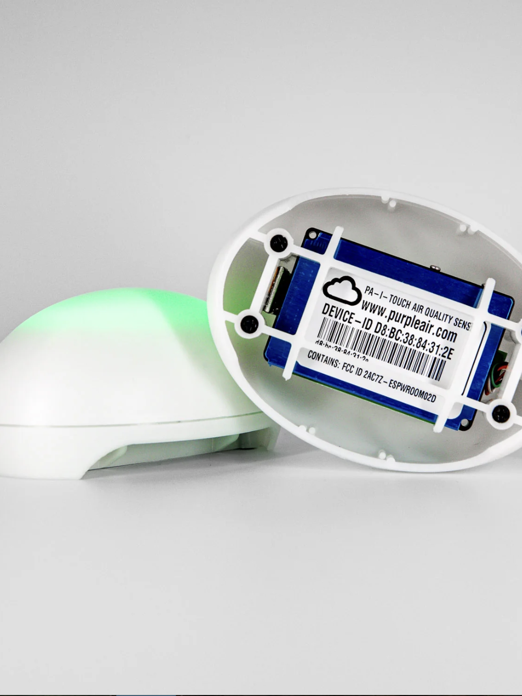 A white, oval air quality sensor with a digital display inside, showing a device ID label. 