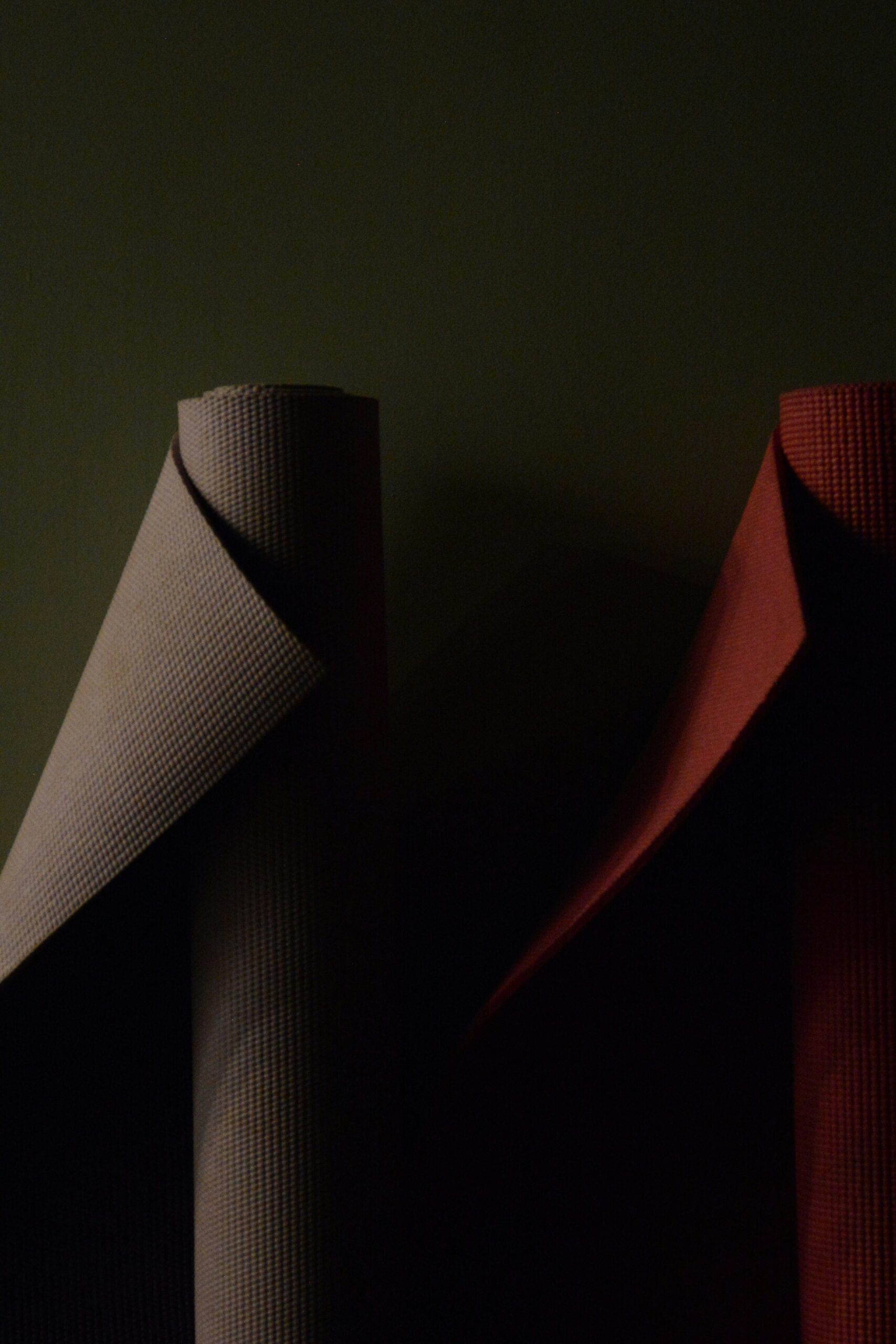 Two vertical rolls of textured fabric, one gray and one red, stand against a dark background.